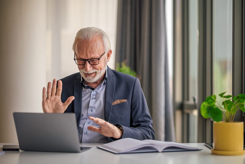 Elderly businessman greeting while video conferencing on laptop about Medicare