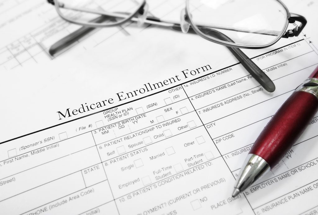 Medicare Enrollment Form document with glasses and pen
