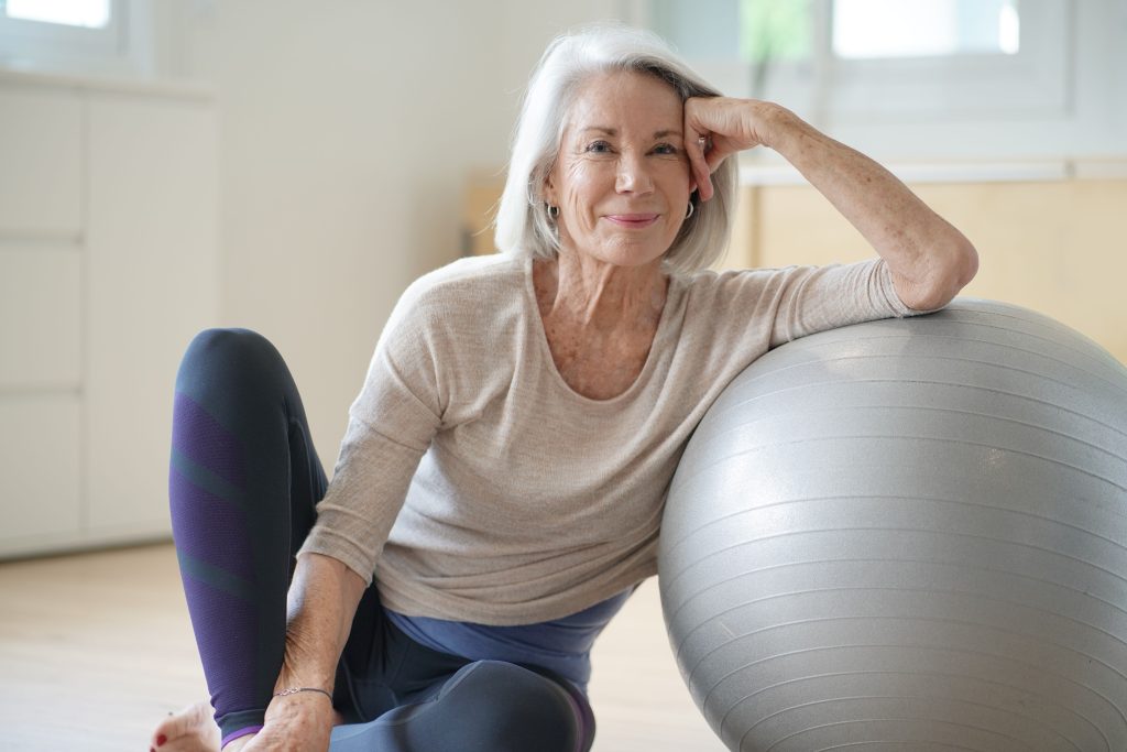 Medicare Benefits Retiree enjoying wellness activities Smiling elderly woman resting on a swiss ball at home